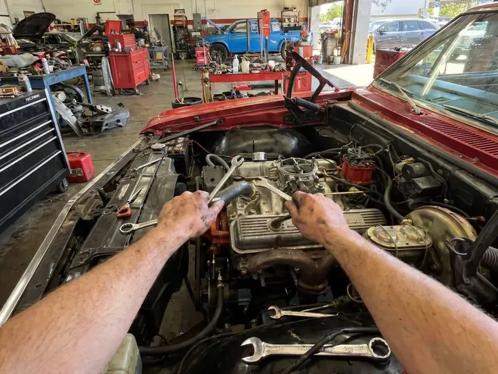 Hands with a tool in the engine of a car